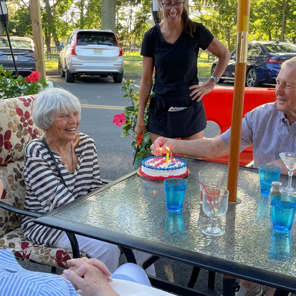 Friends celebrate around a patio table with a birthday cake, colorful drinks, and a server nearby.