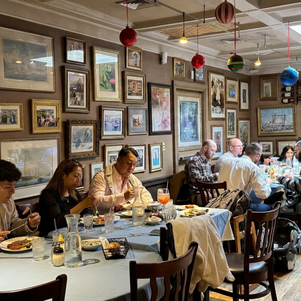 Diners enjoy meals in a warmly lit restaurant filled with framed artwork, mirrors, colorful hanging ornaments, and white tablecloths.